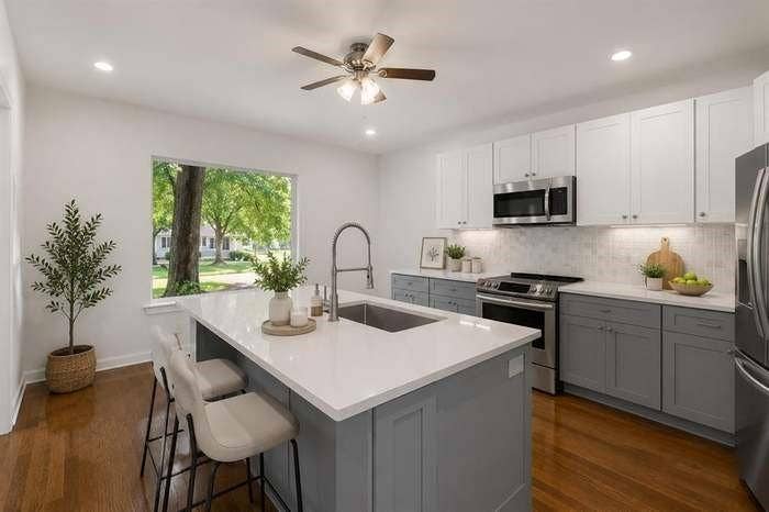 2405 Monroe Street, Commerce, TX 75428 Kitchen featuring wood-finish flooring, a central island with an undermount sink, stainless steel appliances, two-tone cabinetry, and recessed lighting