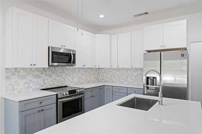 2405 Monroe Street, Commerce, TX 75428 Kitchen featuring two-tone cabinetry, stainless steel appliances, patterned tile backsplash, white countertops, and an undermount sink with a pull-down faucet