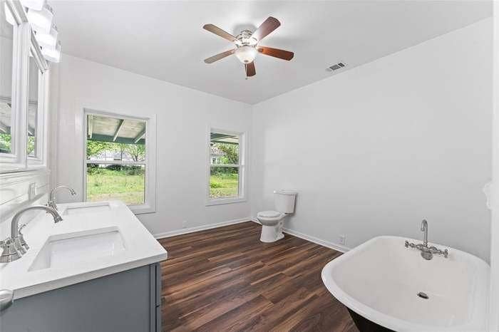 2405 Monroe Street, Commerce, TX 75428 Freestanding soaking tub, wood-finish flooring, dual basin vanity with white countertop, ceiling fan with integrated lighting, and multiple windows