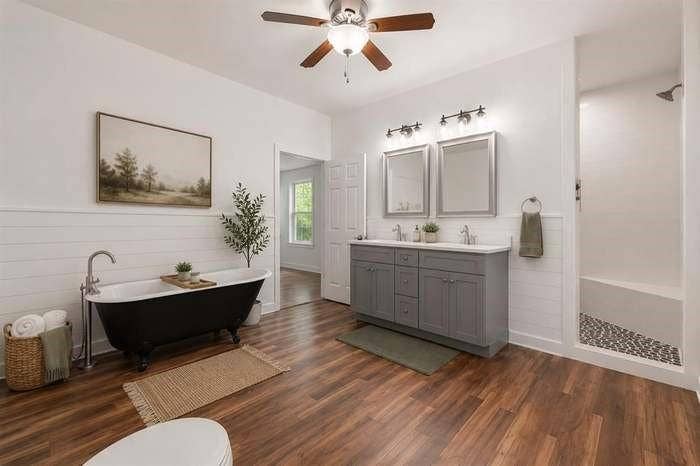2405 Monroe Street, Commerce, TX 75428 Freestanding black clawfoot tub, dual vanity with shaker-style cabinetry, walk-in shower with river rock tile, wood-finish flooring, and a ceiling fan