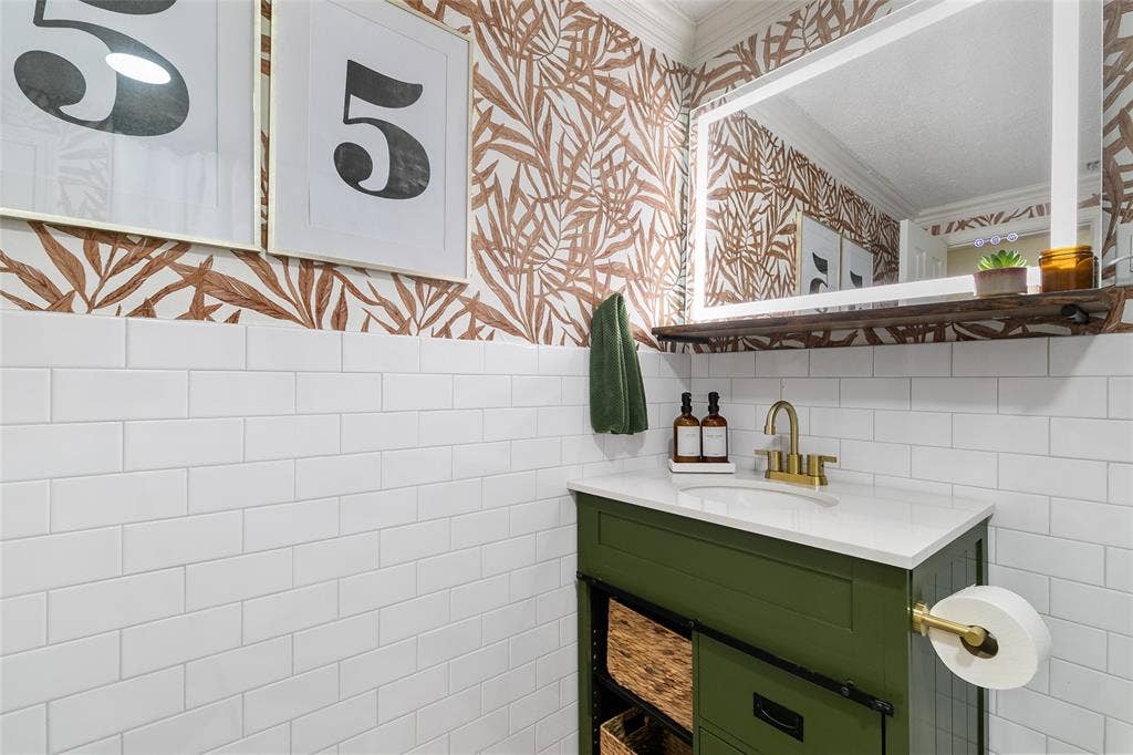 214 Short Street, McKinney, TX 75069 White subway tile wainscoting, green vanity with white countertop, gold-tone faucet, large framed mirror, and decorative wall covering
