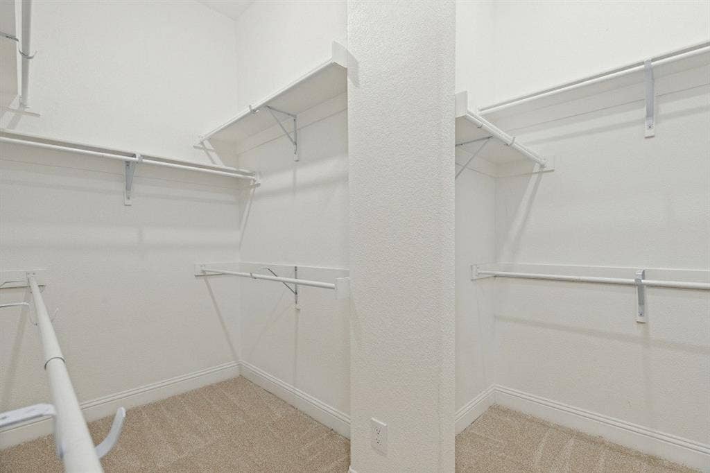 Built-in closet shelving, hanging rods, light-toned carpeting, and a neutral wall finish