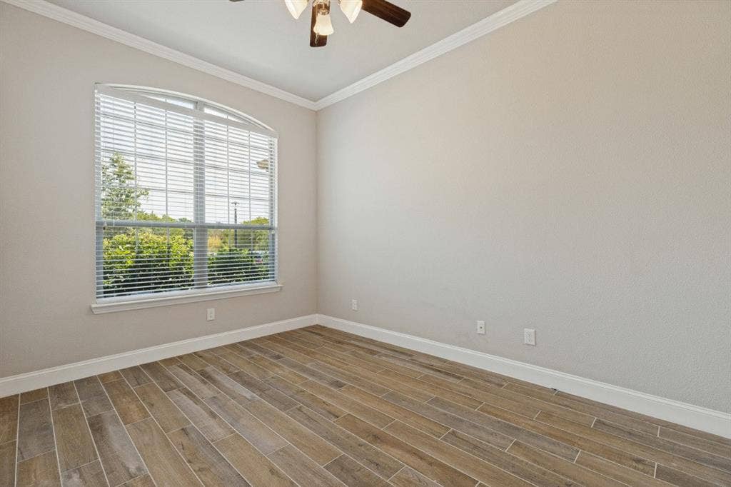Arched window with blinds, wood-finish flooring, ceiling fan, and crown molding