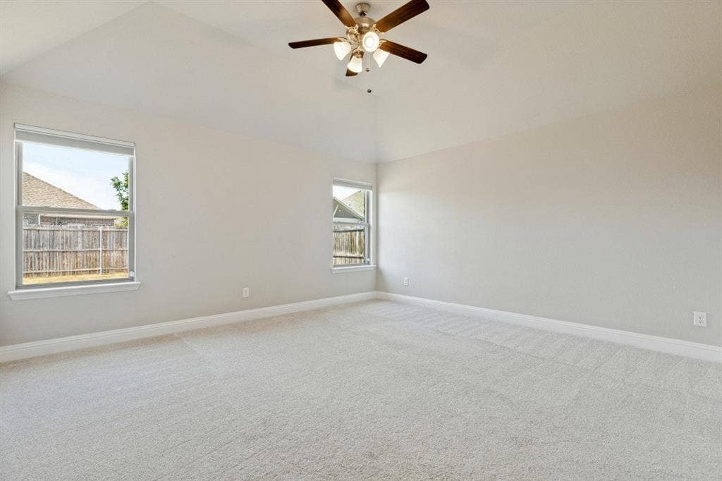 Vaulted ceiling with a ceiling fan, light-toned carpeting, and multiple windows