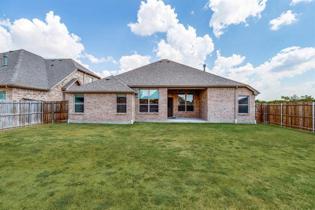 Expansive backyard featuring a manicured lawn, brick exterior, fenced perimeter, and a concrete patio