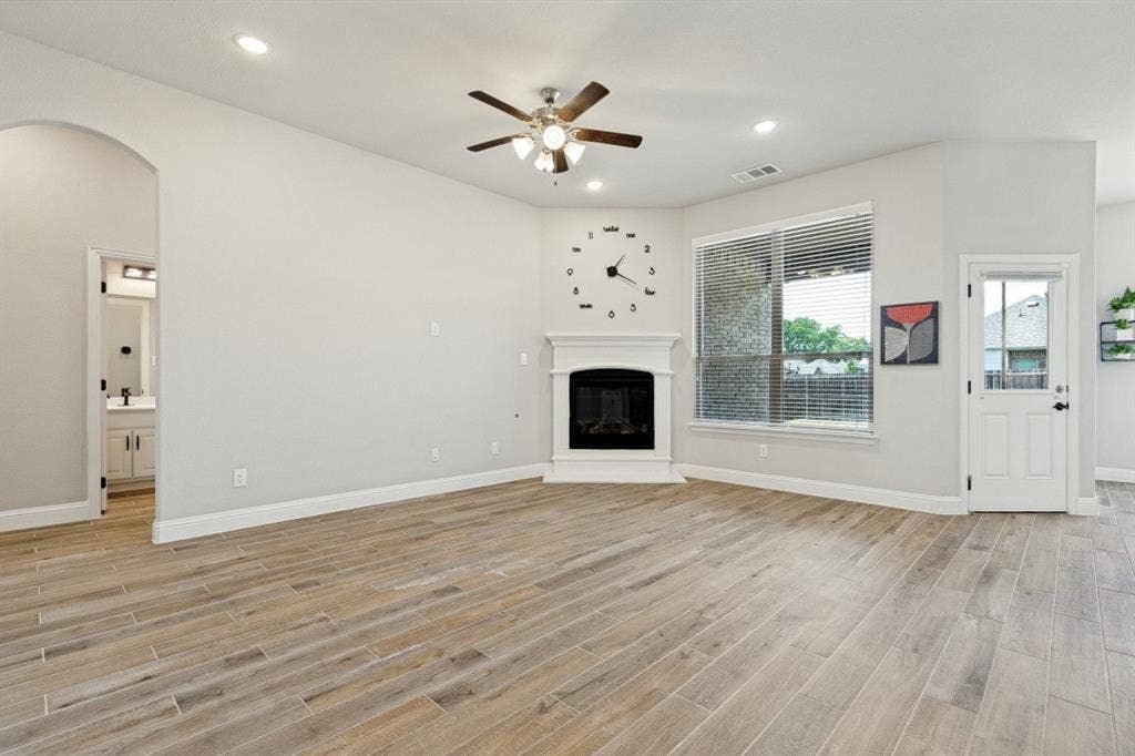 Spacious room featuring wood-finish flooring, a corner fireplace with a white mantel, recessed lighting, and an arched doorway. The entire main part of the home has the porcelain ceramic wood plank tile, very difficult to damage and a breeze to keep spotless.