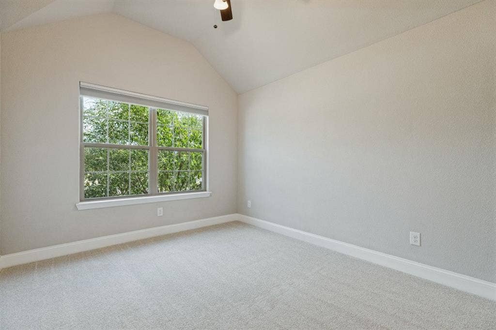 Vaulted ceiling, ceiling fan, large window with natural light, light-toned carpet, and neutral wall tones