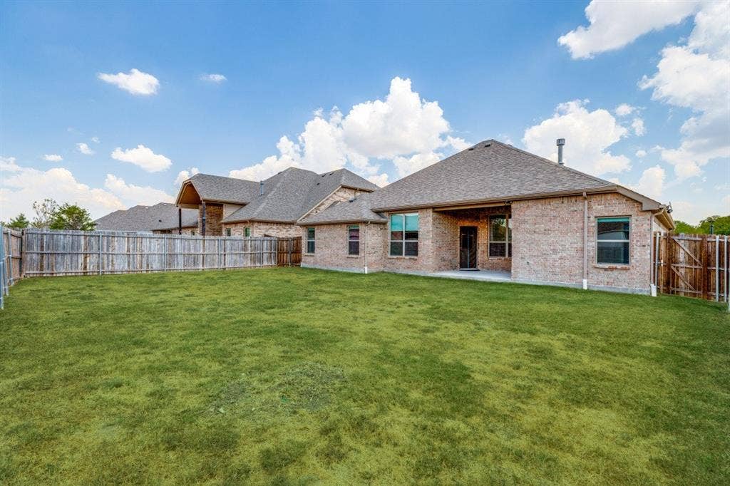 Expansive backyard featuring a manicured lawn, full privacy fencing, and a covered patio area