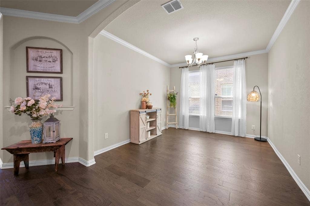 Arched entryway with a recessed wall niche, wood-finish flooring, crown molding, and a chandelier