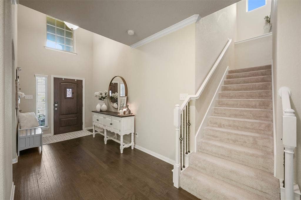 Two-story entryway with wood-finish flooring, a dark wood-paneled door with an arched top, and a carpeted staircase featuring a white railing and wrought iron balusters