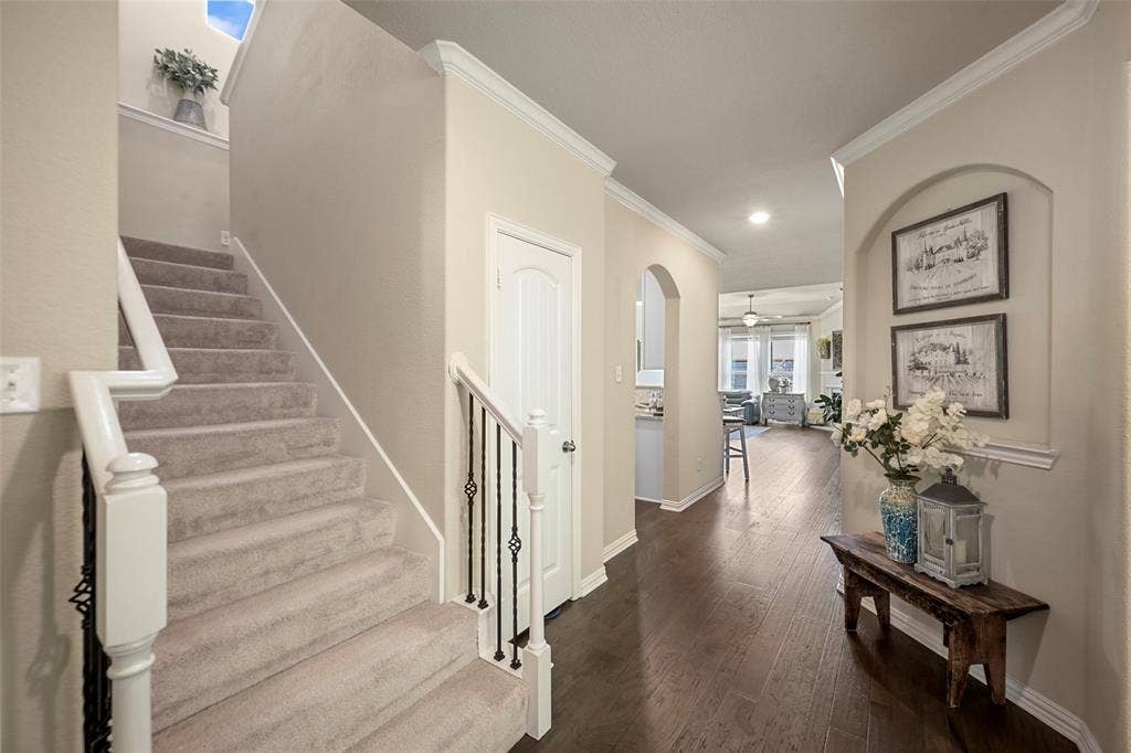 Hardwood-style flooring extends through the hallway, complemented by a carpeted staircase with white balusters and wrought iron spindles
