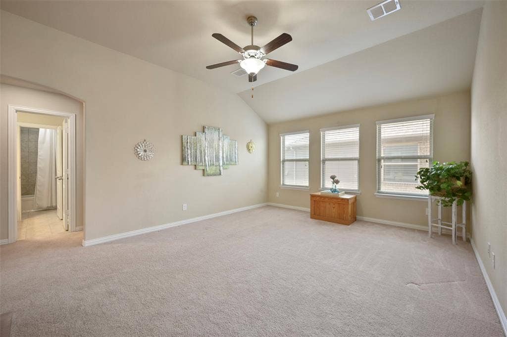Spacious carpeted room featuring a vaulted ceiling with a ceiling fan, multiple windows with blinds, and an arched doorway