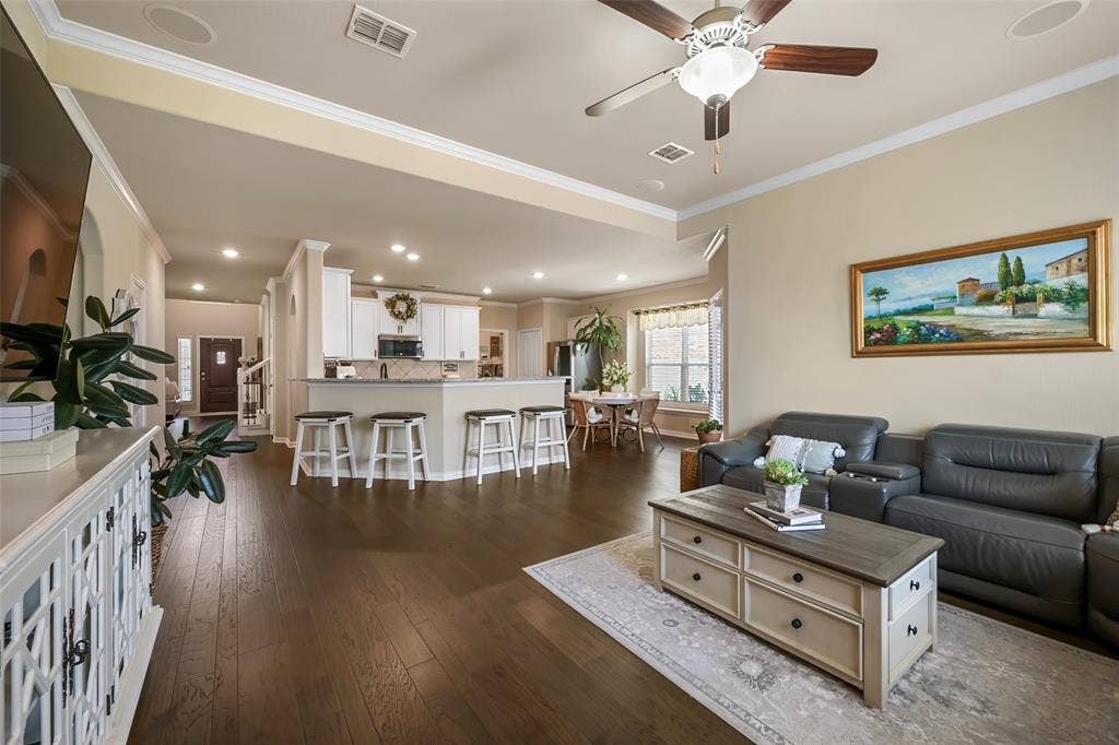 Open-concept living area featuring wood-finish flooring, recessed lighting, crown molding, and a kitchen with white cabinetry and a built-in breakfast bar