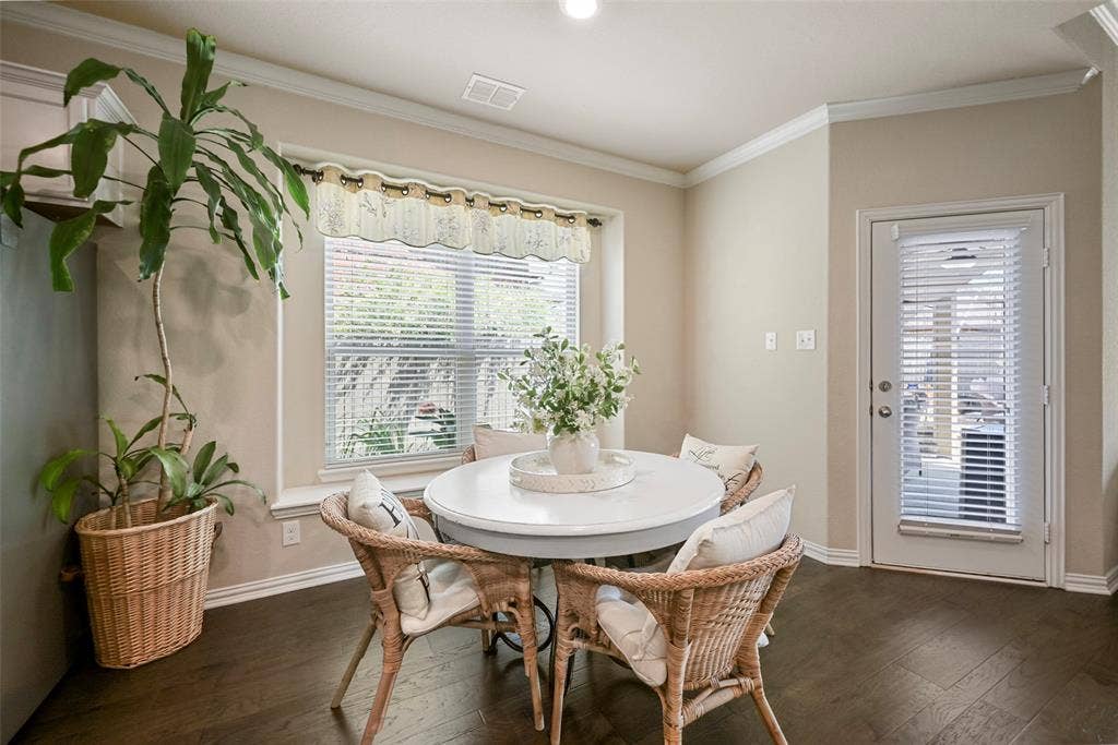 Wood-finish flooring, crown molding, a large window with blinds, and a door with integrated blinds