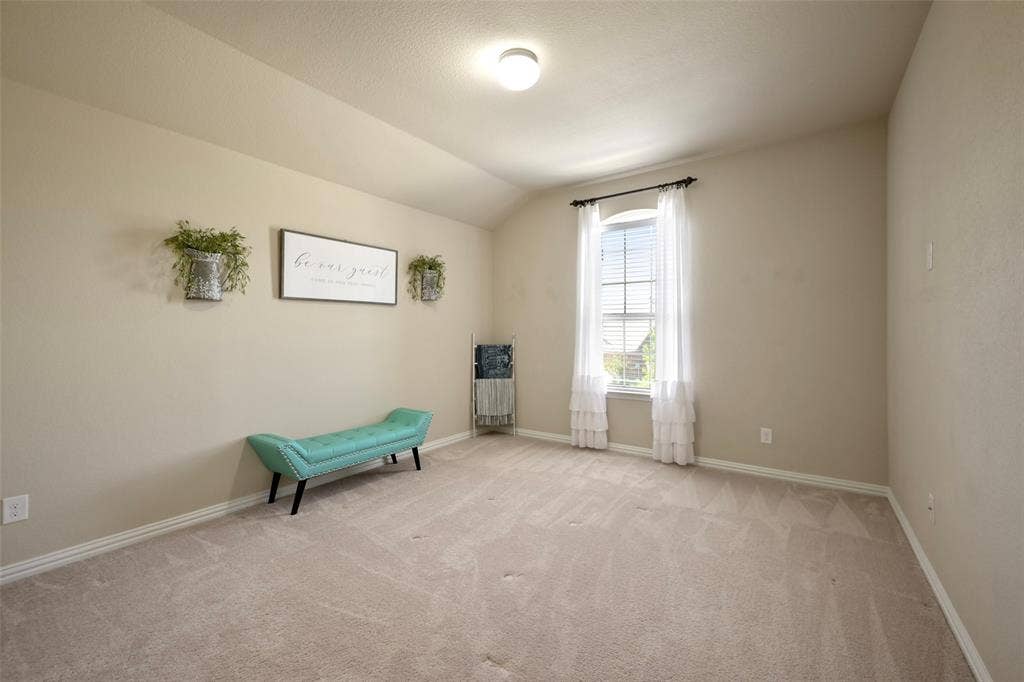 Spacious room featuring vaulted ceilings, neutral-toned walls, and an arched window