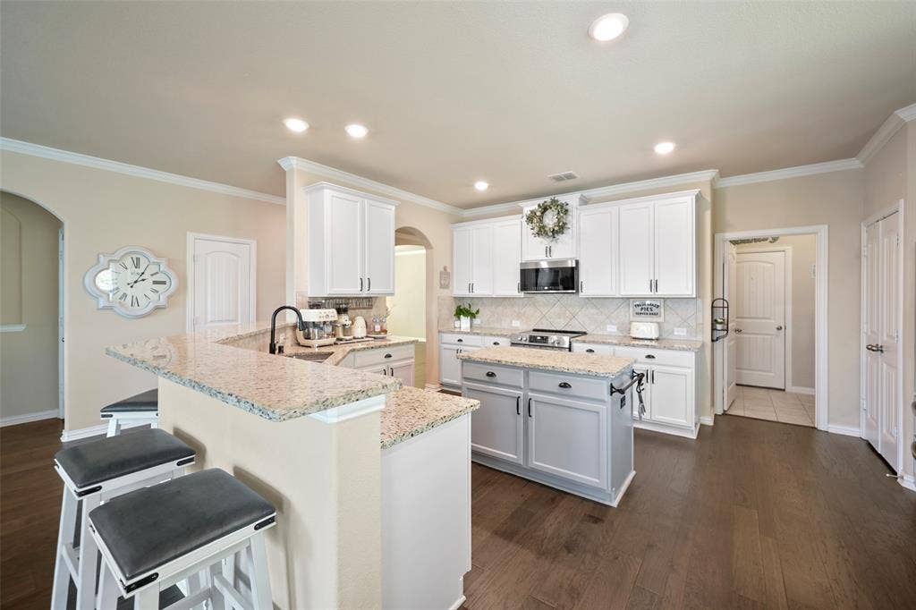 Kitchen featuring a center island, white cabinetry, granite-finish countertops, subway tile backsplash, and wood-finish flooring