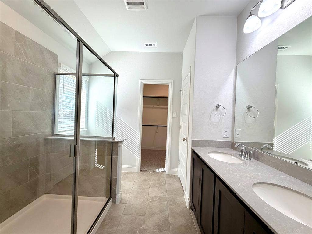 3806 Chicory Court, Melissa, TX 75454 This primary bathroom features a spacious, modern walk-in shower finished with a clean clear glass enclosure and elegant, durable tile surround, perfectly complemented by a functional and stylish dual-sink vanity arrangement.