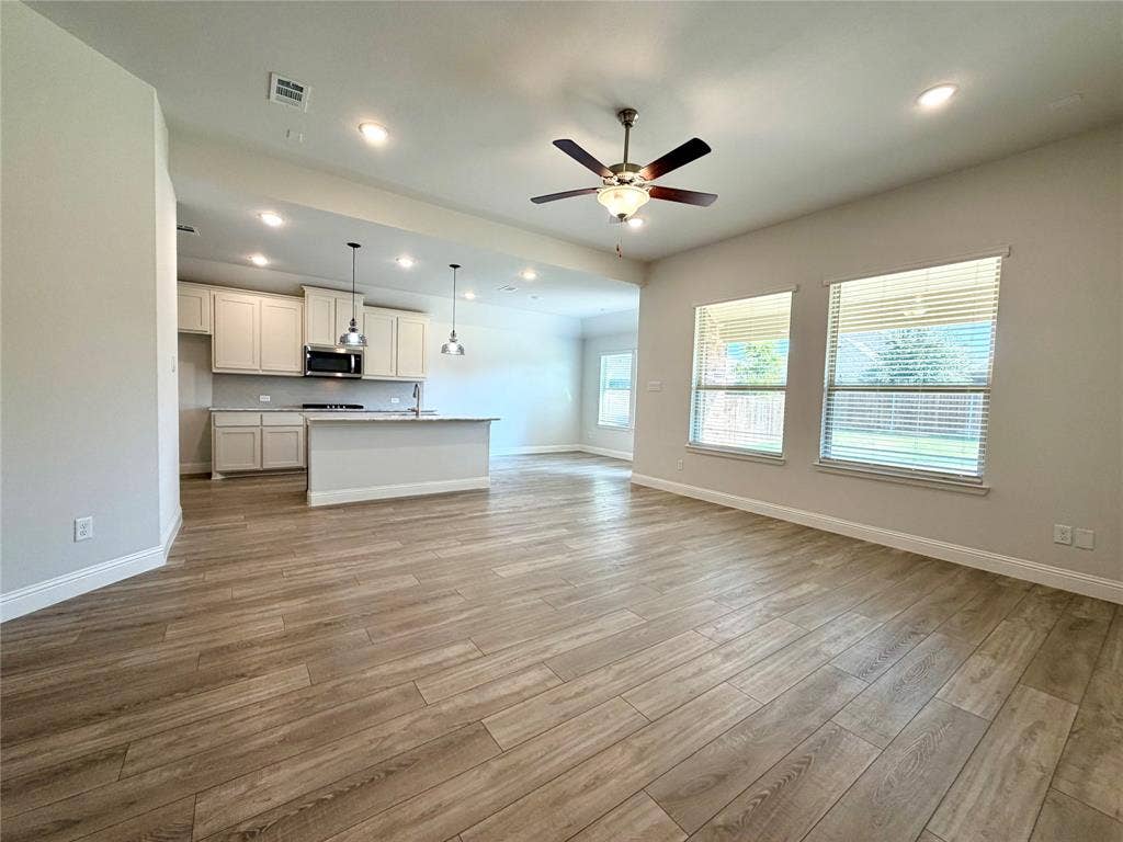 3806 Chicory Court, Melissa, TX 75454 This spacious living room is highlighted by premium luxury vinyl plank (LVP) flooring, energy-efficient recessed lighting, and a ceiling fan. The design features an airy, open-concept floor plan that flows seamlessly into the kitchen and dining area, perfectly complemented by a expansive wall of windows that floods the space with abundant natural light.