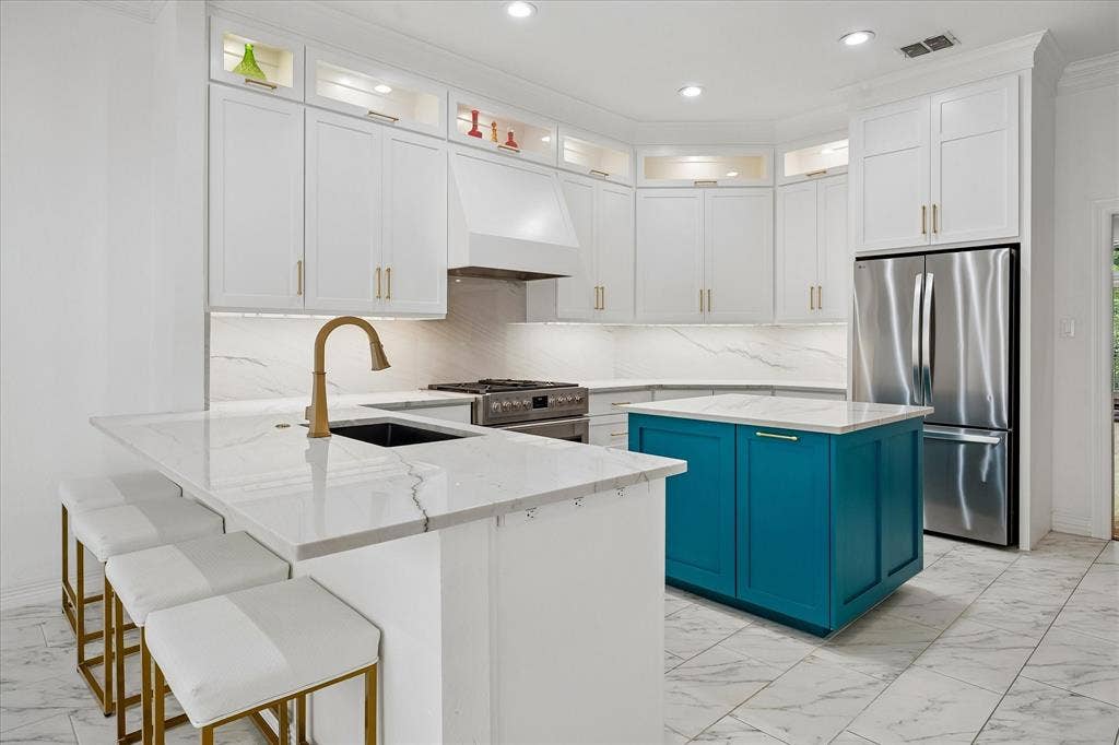 White cabinetry with gold-tone hardware, recessed lighting, stainless steel appliances, a center island with a contrasting base, and a kitchen island with a built-in sink
