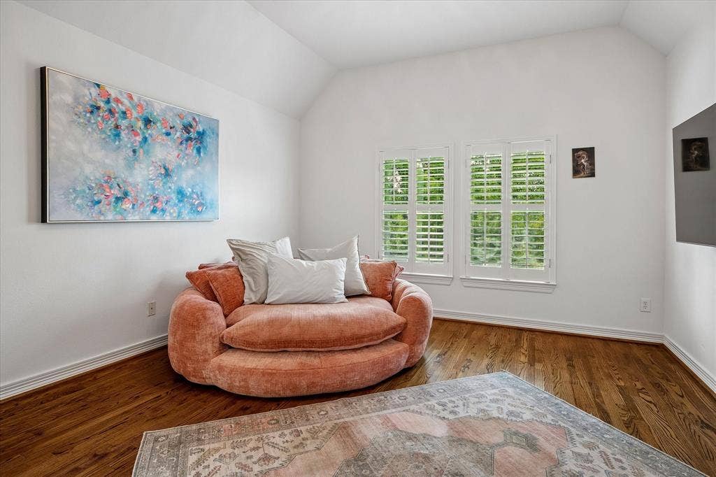 Vaulted ceiling, hardwood flooring, white wall finishes, two windows with plantation shutters, and white trim