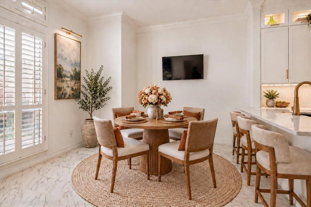 White plantation shutters, white marble-patterned flooring, built-in cabinetry with under-cabinet lighting, and a kitchen island with seating