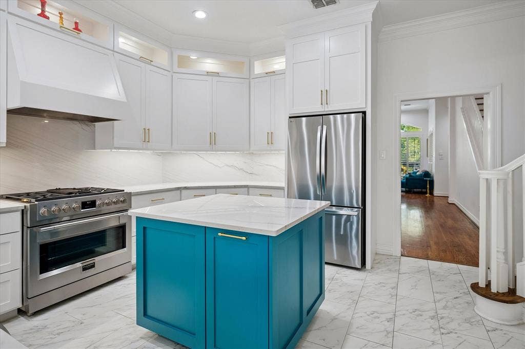 Modern kitchen featuring white cabinetry, a teal island with a white countertop, stainless steel appliances, and white marble-look flooring