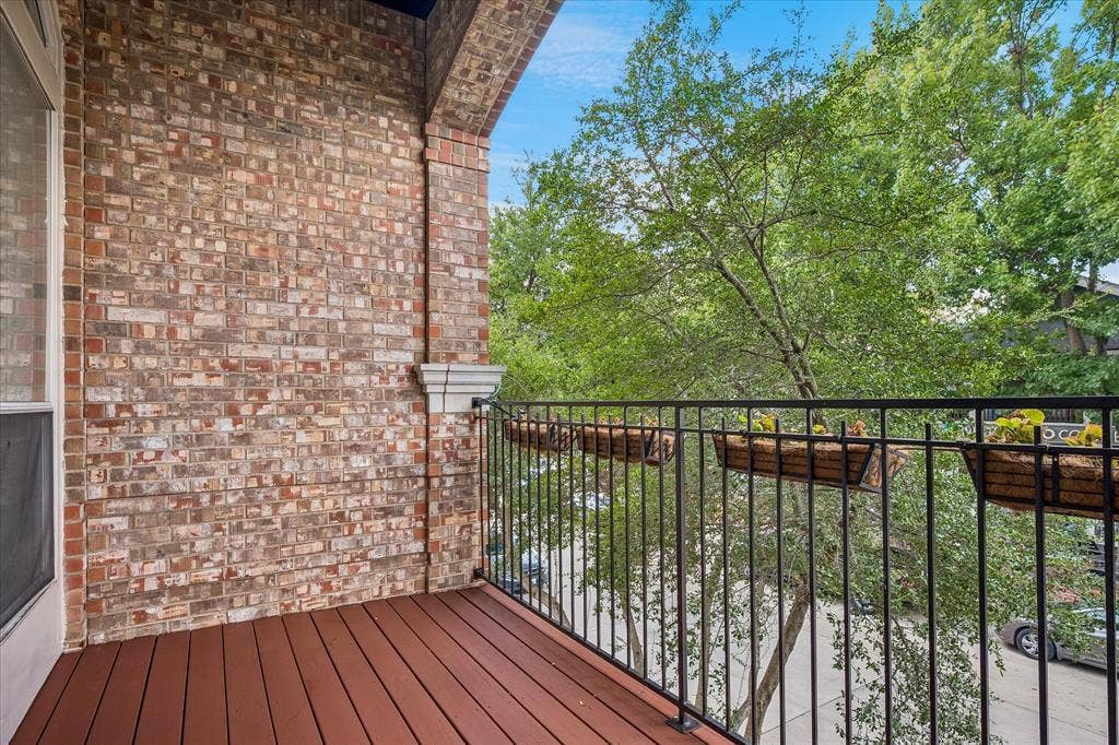 Balcony featuring a brick exterior wall, dark wood-finish flooring, and a black wrought-iron railing