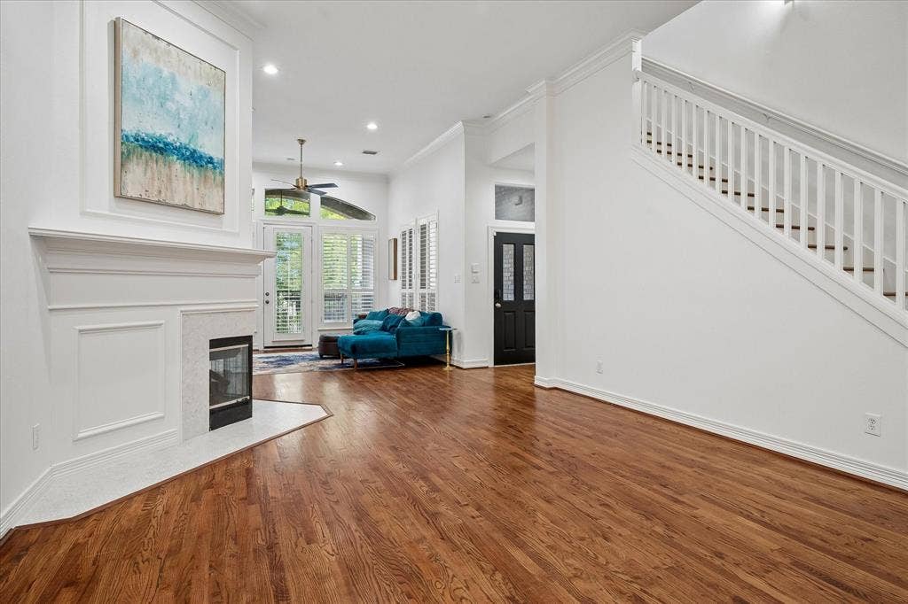 Hardwood flooring, white painted walls, white fireplace with stone surround, white staircase with balusters, and a dark paneled door