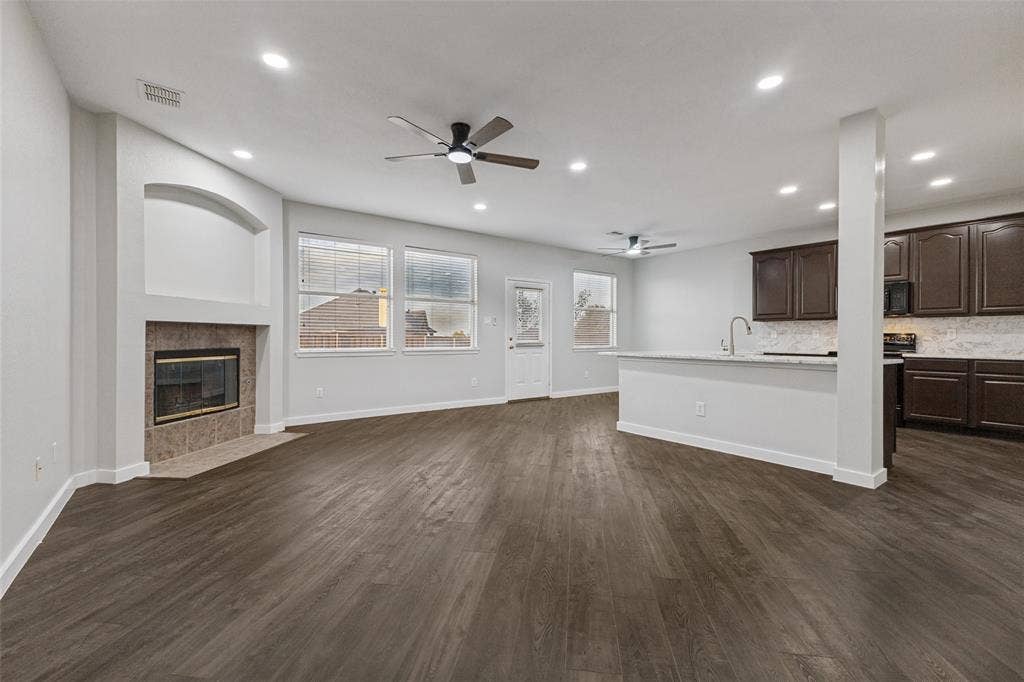 4215 Maidstone Drive, Garland, TX 75043 Spacious living area featuring wood-finish flooring, a tiled fireplace with an arched niche, recessed lighting, and ceiling fans