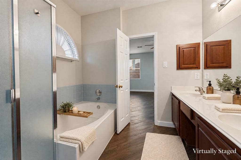4215 Maidstone Drive, Garland, TX 75043 Primary bathroom featuring a built-in tub, a frosted glass shower enclosure, a double vanity with an integrated countertop, and wood-finish flooring