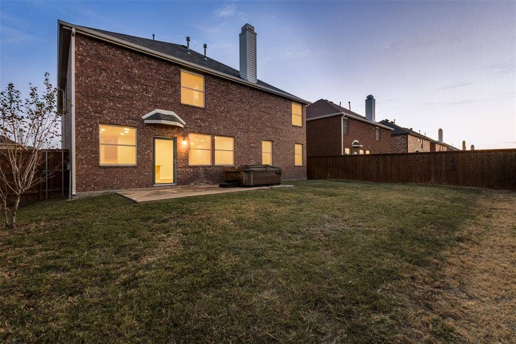 4215 Maidstone Drive, Garland, TX 75043 Brick exterior with multiple windows, concrete patio, and a privacy fence enclosing a grassy yard
