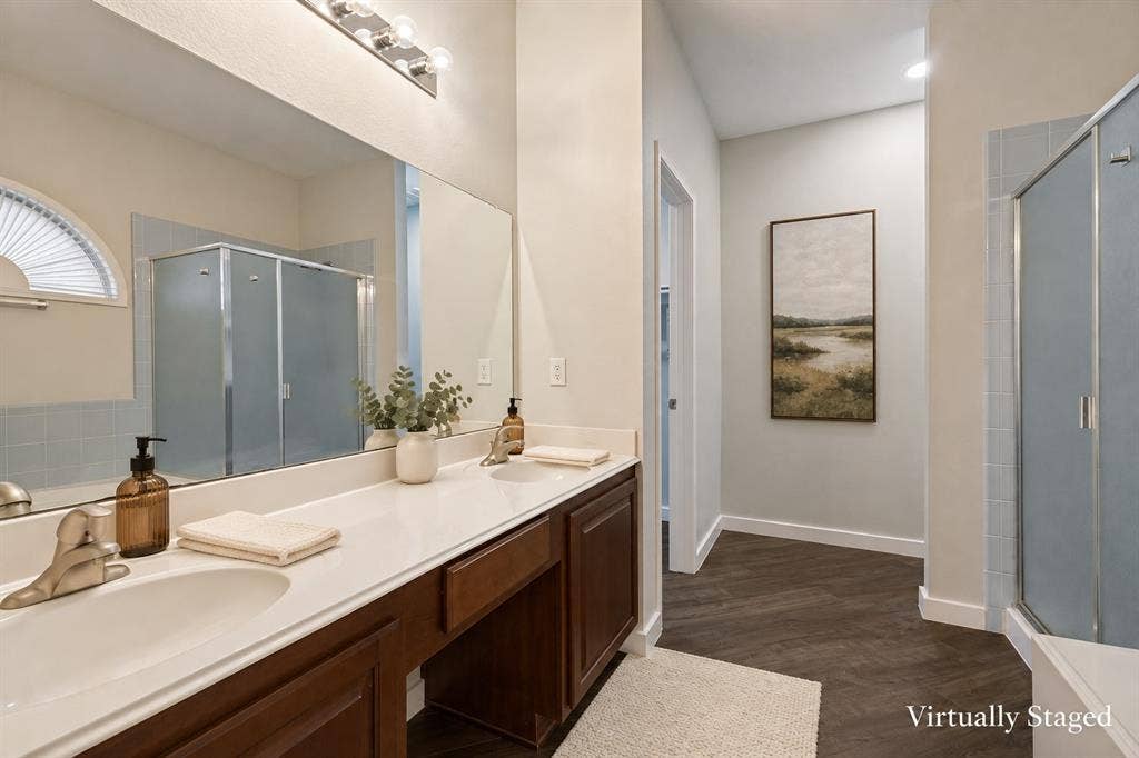 4215 Maidstone Drive, Garland, TX 75043 Primary bathroom featuring a built-in tub, a frosted glass shower enclosure, a double vanity with an integrated countertop, and wood-finish flooring expansive mirror, and a three-light fixture
