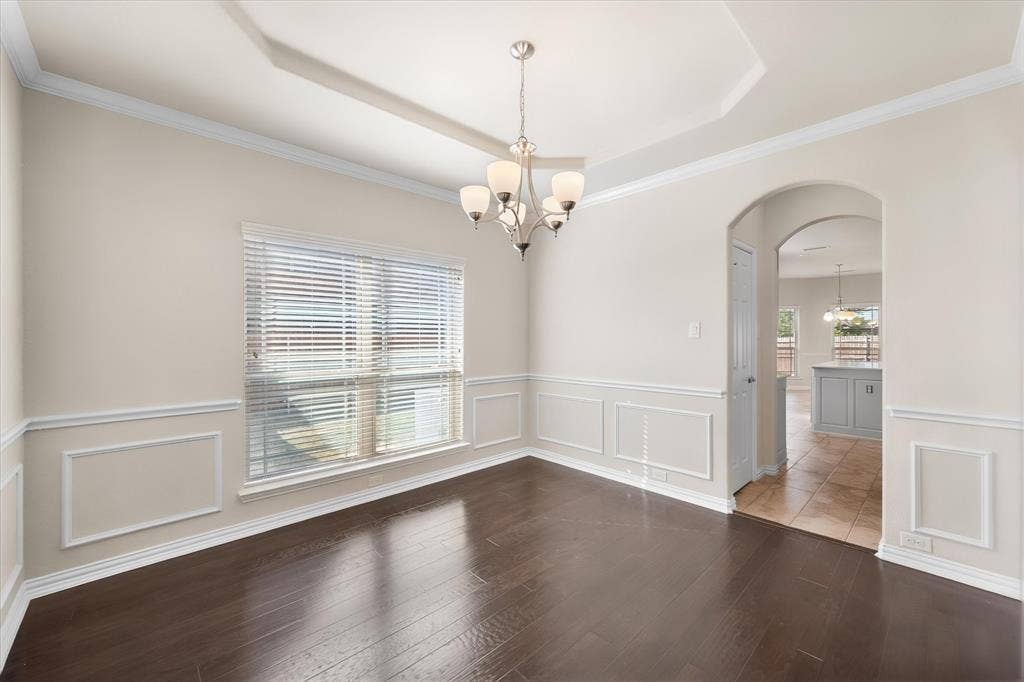 Tray ceiling with a decorative chandelier, crown molding, and wainscoting