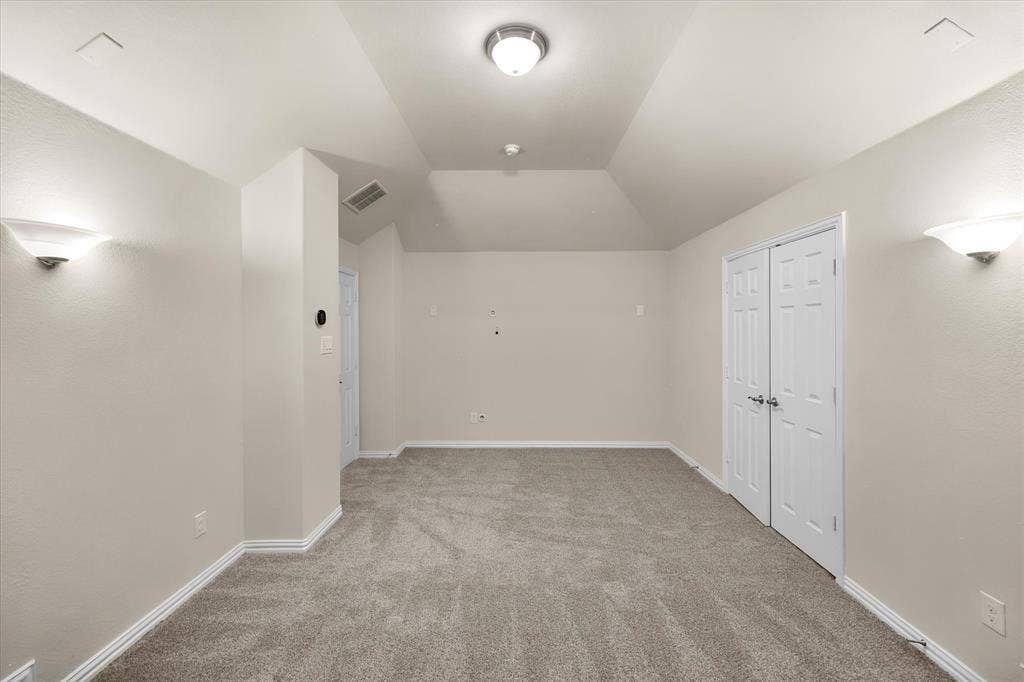 Vaulted ceiling with an overhead light fixture, carpeted flooring, and wall-mounted sconces