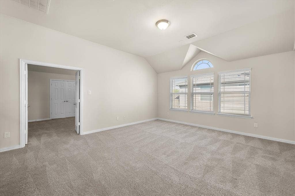 Spacious room with vaulted ceilings, neutral-toned carpeting, multiple windows including an arched transom, and a flush mount ceiling light