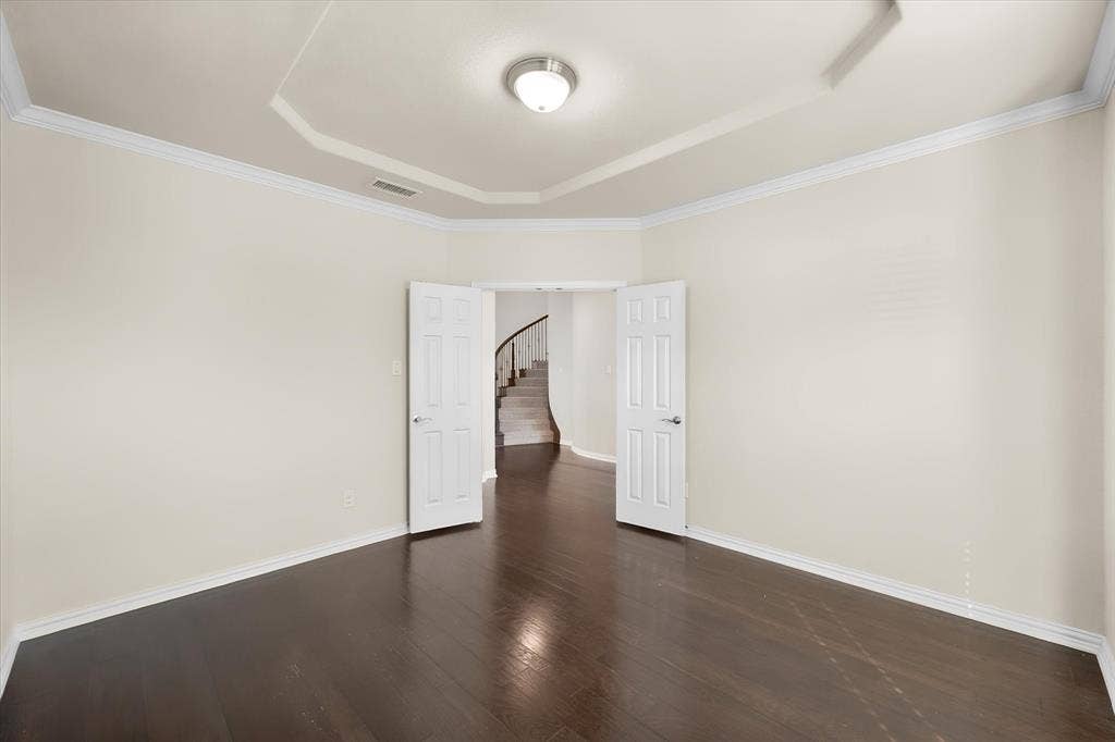 Recessed ceiling with crown molding, dark wood-finish flooring, and white paneled doors