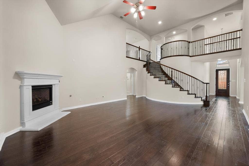 Spacious living area featuring a fireplace with a white mantel, high vaulted ceilings, and dark wood-finish flooring