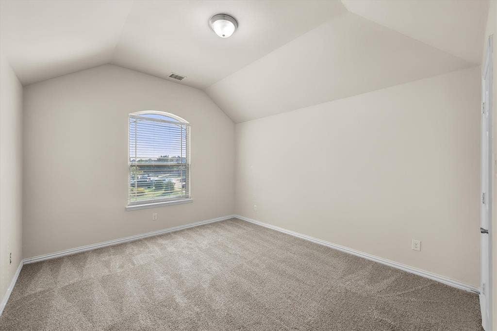 Arched window with blinds, vaulted ceiling, neutral wall tones, flush mount lighting, and carpet flooring
