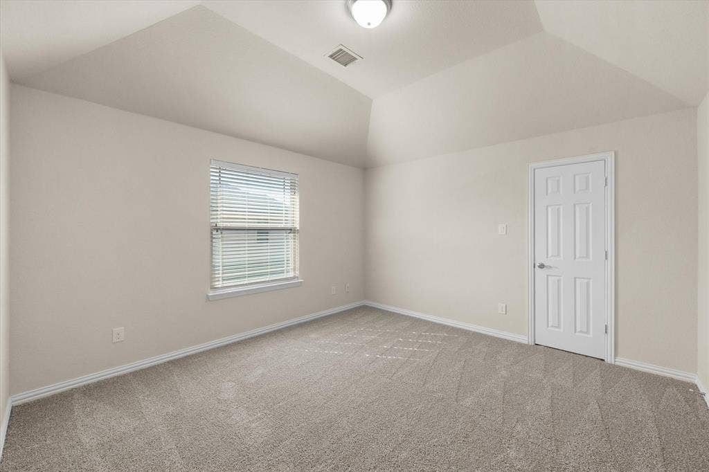 Vaulted ceiling, neutral wall tones, window with blinds, carpet flooring, and a paneled door