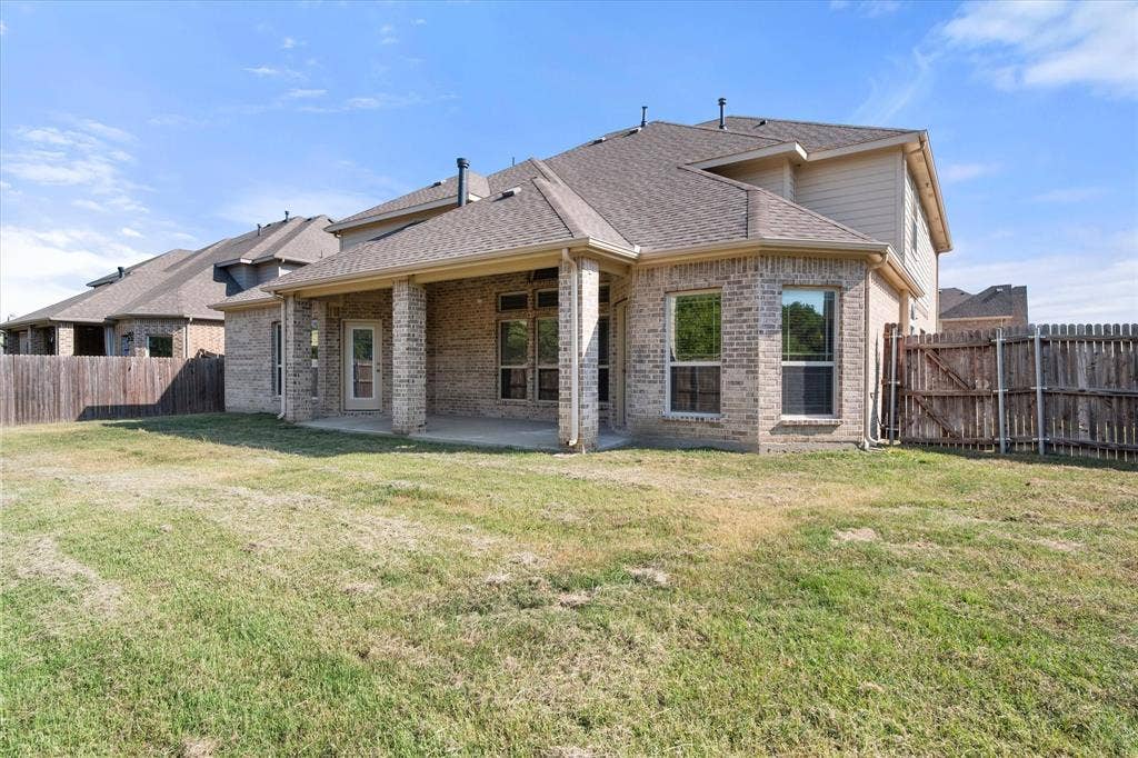 Brick exterior with a covered patio, multiple windows, and a wood privacy fence