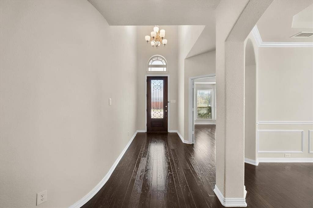 Entryway featuring wood-finish flooring, a decorative glass front door with an arched transom, a chandelier, and arched doorways