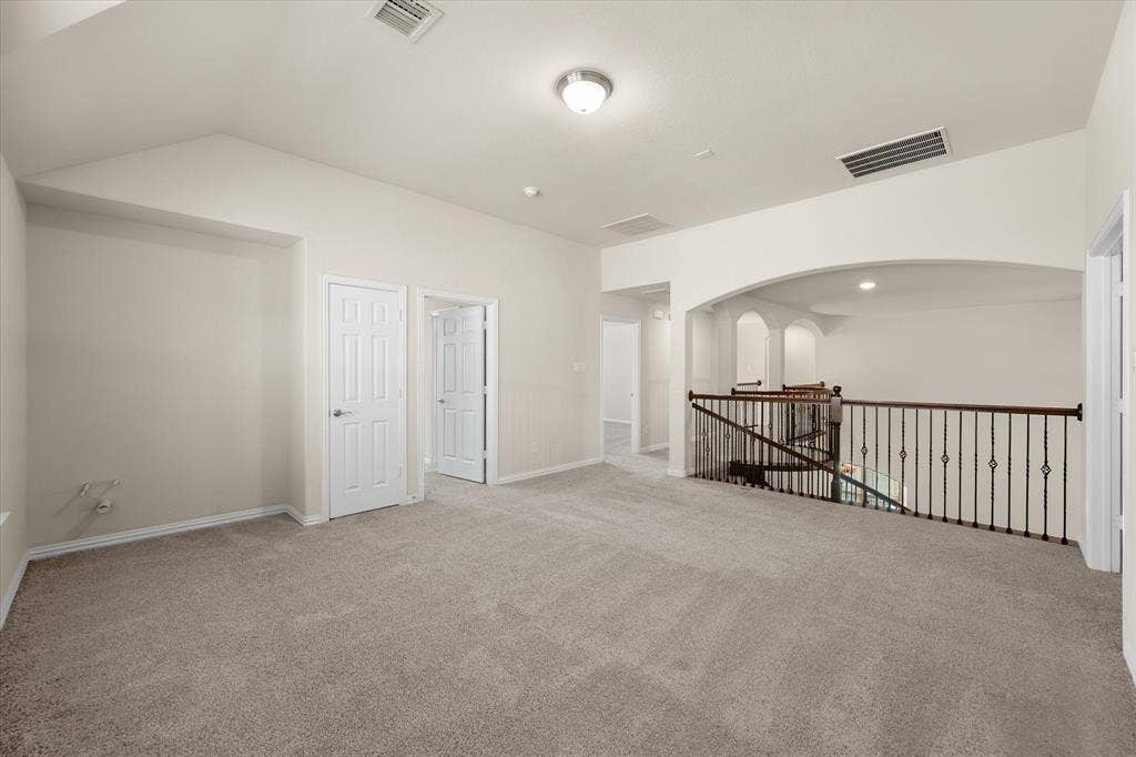 Carpeted open area featuring a vaulted ceiling and a wrought iron and wood railing