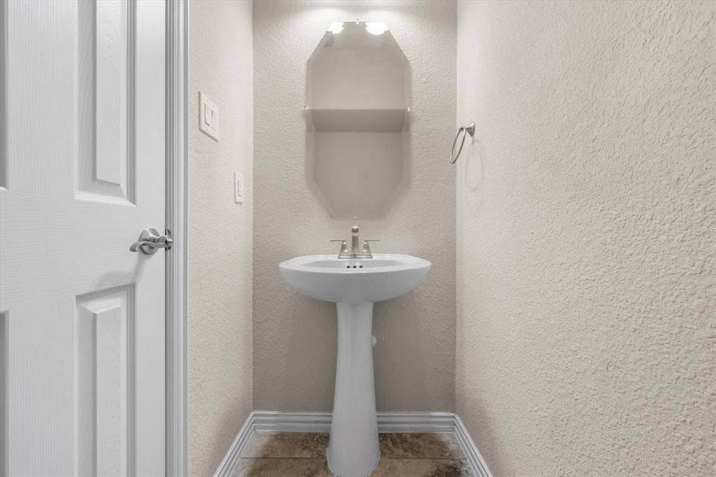Pedestal sink with chrome faucet, textured walls, overhead lighting, and wood-finish flooring