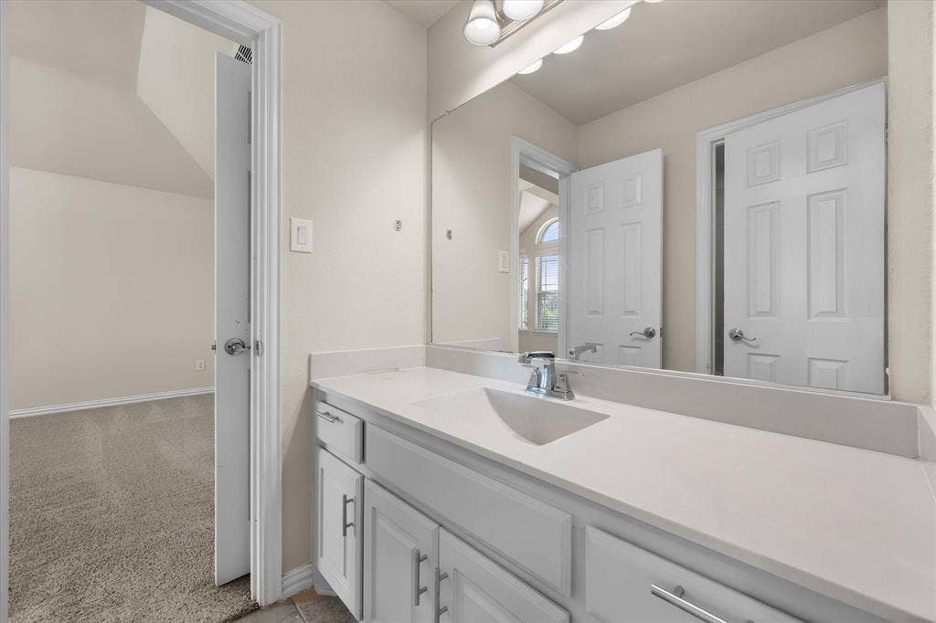 Vanity with integrated sink, chrome faucet, white cabinetry, and wall-mounted mirror