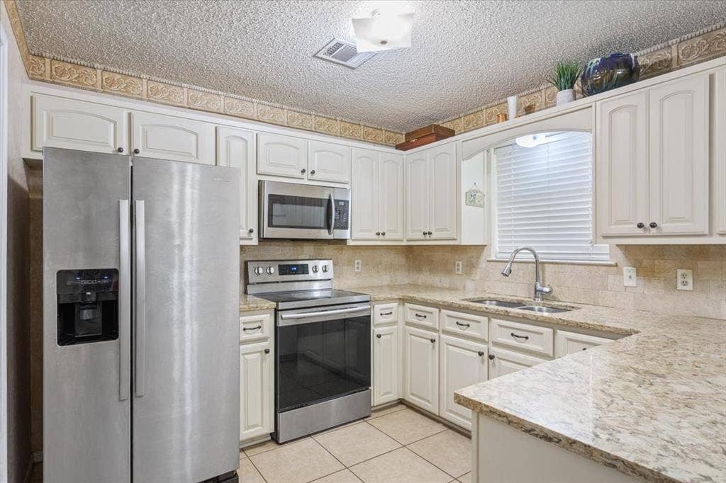 Kitchen featuring white cabinetry, stainless steel appliances, a double basin sink, and light-toned countertops