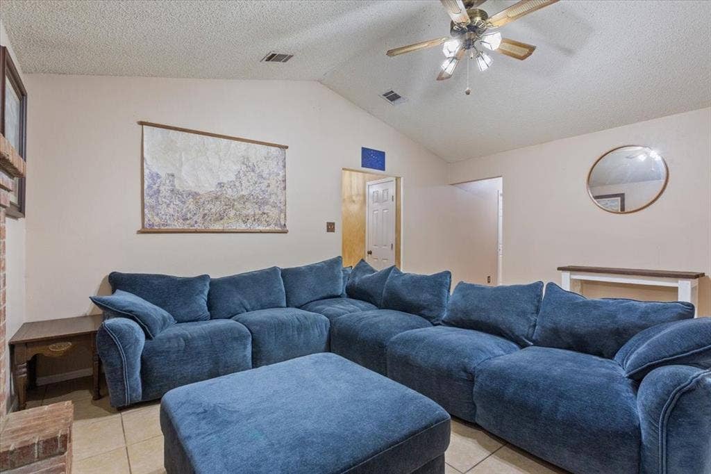Vaulted ceiling with an attached ceiling fan, tile flooring, and a brick-finish fireplace