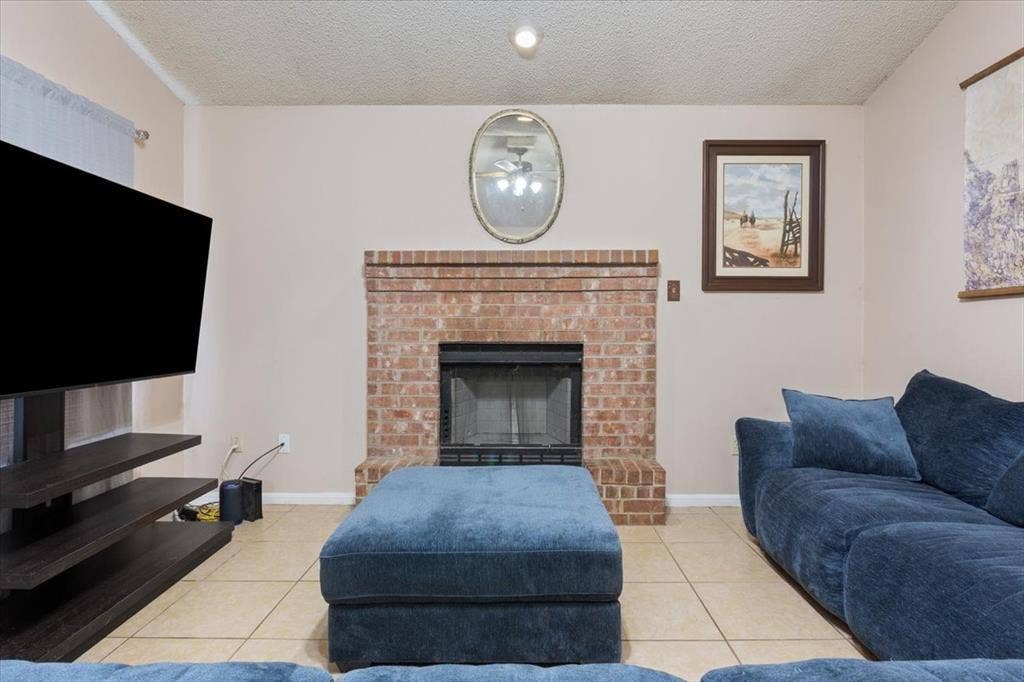 Brick fireplace with a black firebox and hearth, recessed ceiling lighting, and light-toned tile flooring