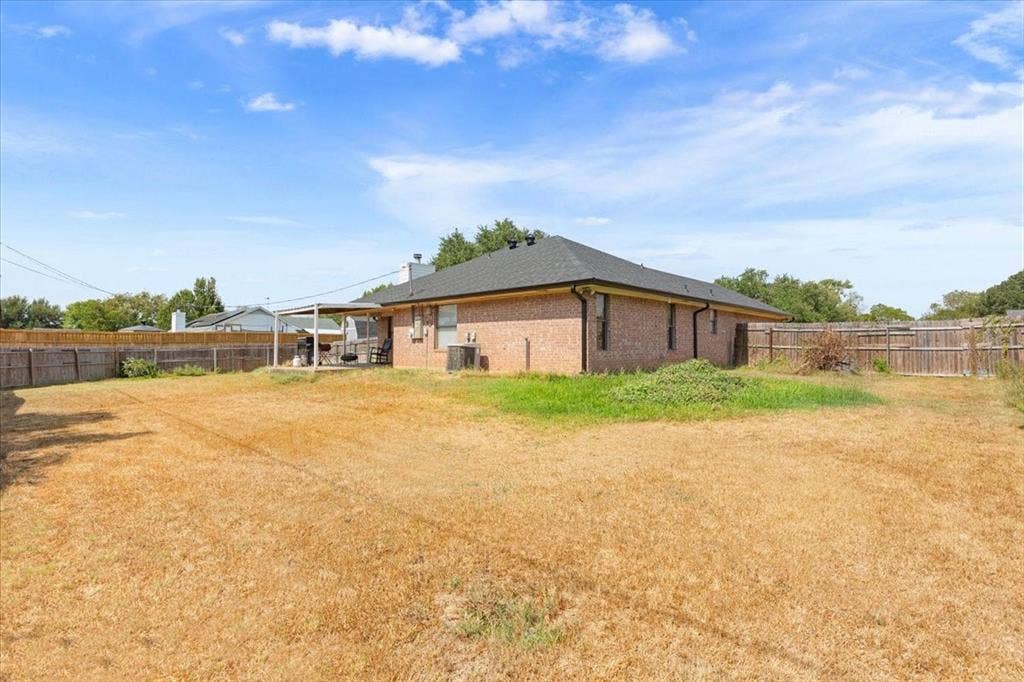Brick exterior with a dark shingle roof, a covered patio, and a privacy fence