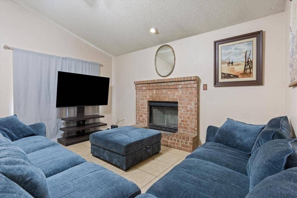 Vaulted ceiling, brick fireplace, built-in fireplace screen, tile flooring, window with curtain rod