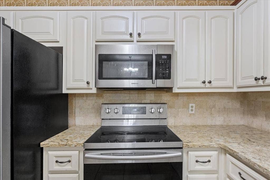 White cabinetry with dark hardware, stone-look countertops, and a tiled backsplash